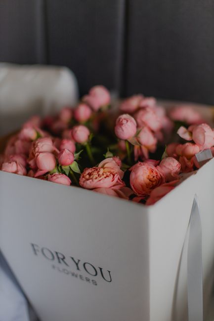 A white rectangular box with the label 'FOR YOU FLOWERS' contains a lush arrangement of fresh pink peonies, some with partially opened petals revealing soft, ruffled centers. The flowers are densely p